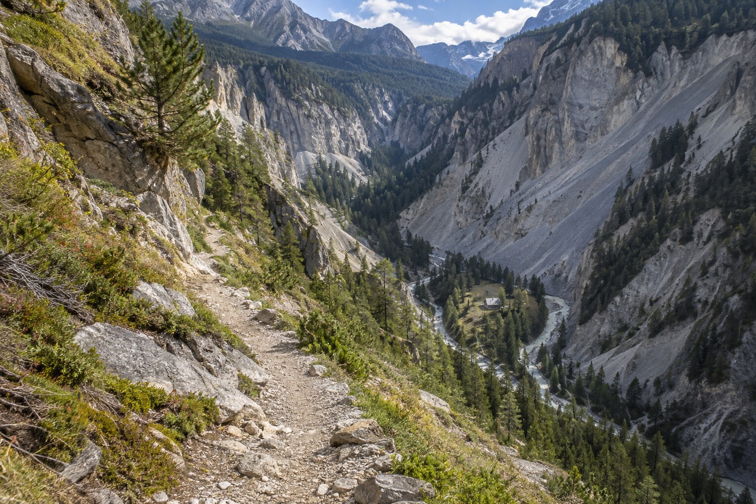 Hiking trail descending toward the Cluozza gorge with the Chamanna Cluozza hut visible below